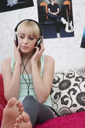 Teenage girl (16-17) sitting on bed listening to musicの写真素材