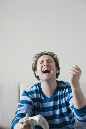 Man holding computer game controls laughing on sofaの写真素材