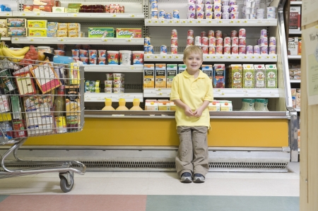 Young boy standing by fridge counter of supermarketの写真素材