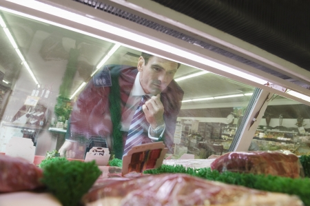 Mature man looks through glass of meat counter in supermarketの写真素材