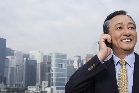 Middle-aged business man talking on mobile office buildings in backgroundの写真素材
