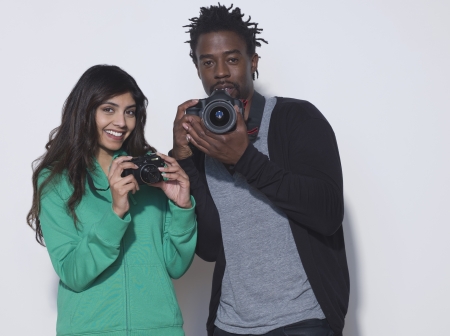 Studio shot of young woman and mid adult man holding digital camerasの写真素材