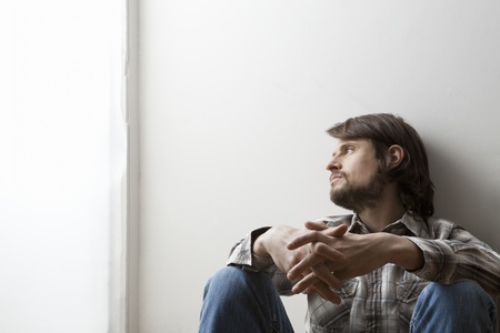 Young man in checked shirt sits with hands clasped against a wallの写真素材