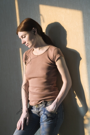 Redhead stands with hand in pocket listening to headphonesの写真素材