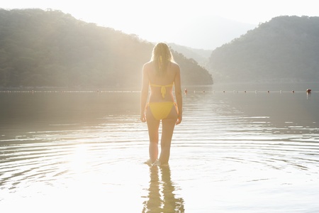 Woman in yellow bikini stands at edge of lakeの写真素材