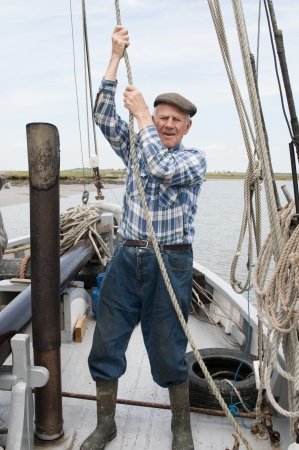 Elderly fisherman pulling rope on deckの写真素材