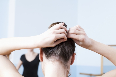 Young woman adjusts hair during ballet classの写真素材