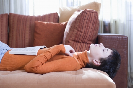 Brunette woman lies on her back with eyes closed and an open bookの写真素材