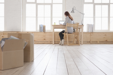 Woman sits at desk in window area of loft apartmentの写真素材