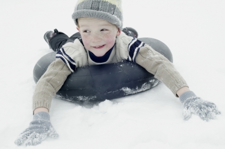 Boy in winter clothing sledging on an inner tyreの写真素材