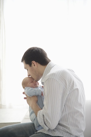 father kisses two week old newborn babies headの写真素材