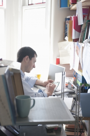 Mid adult man with calculator in home officeの写真素材