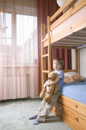 5 year old boy leans on bunk bed holding teddybearの写真素材