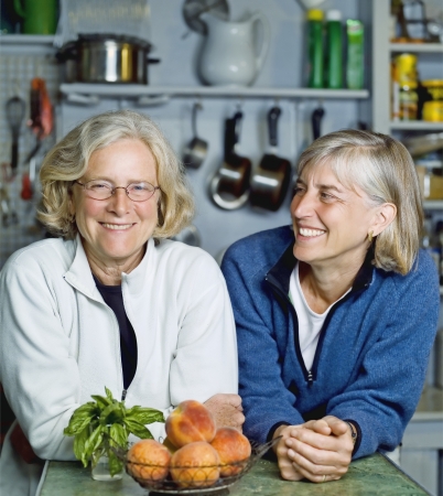 Two mature women lean on kitchen counter smilingの写真素材