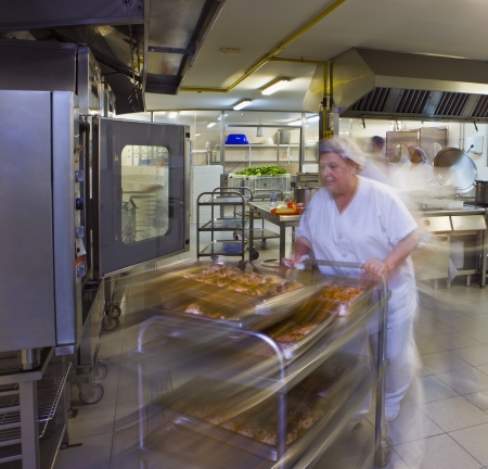 Kitchen porter pushes a trolley of pastriesの写真素材