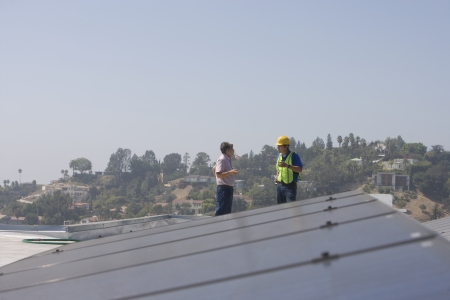 Maintenance workers stand with solar array on rooftop in Los Angeles California