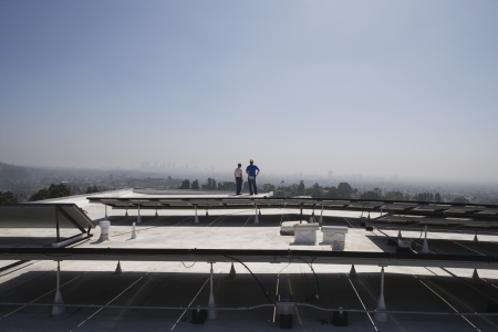 Maintenance workers stand with solar array on rooftop in Los Angeles Californiaの写真素材