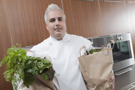 Mid- adult chef with two bags of fresh groceriesの写真素材