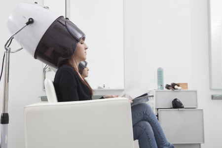 Female client sits under drying hood in hair salonの写真素材