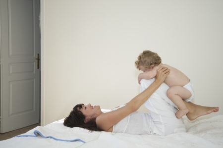 A mother laying down with legs bent holding a toddler on themの写真素材