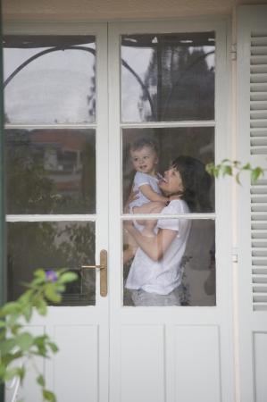 Mother and toddler standing inside a door with glass windowsの写真素材