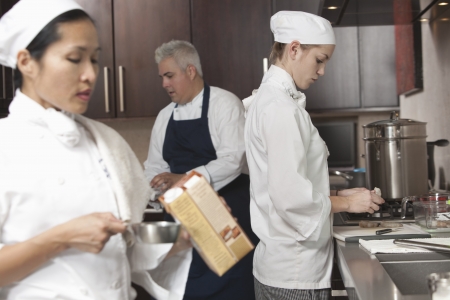 Three chefs work together in busy kitchenの写真素材