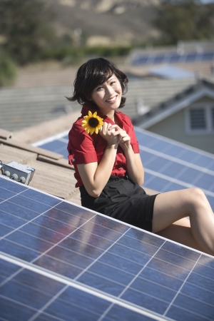 A lady on a solar panalled rooftop holding a sunflowerの写真素材