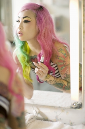 Reflection of a young woman in mirror applying lipstickの写真素材