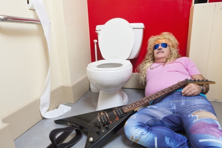 Man lying down in toilet with a guitarの写真素材