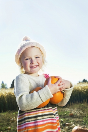 Portrait of a happy girl holding pumpkinsの写真素材