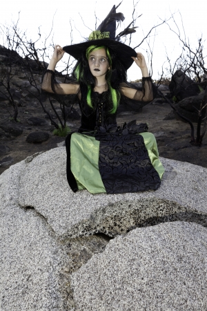 Little young girl costumed as witch sitting on rock looking awayの写真素材