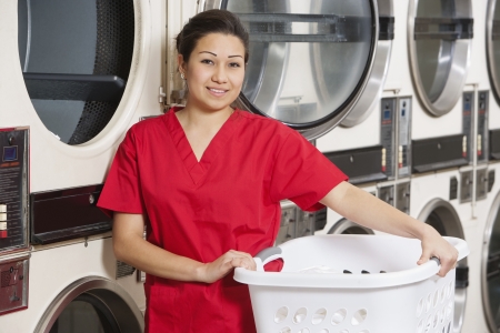 Portrait of a happy woman carrying laundry basket with washing machine in backgroundの写真素材
