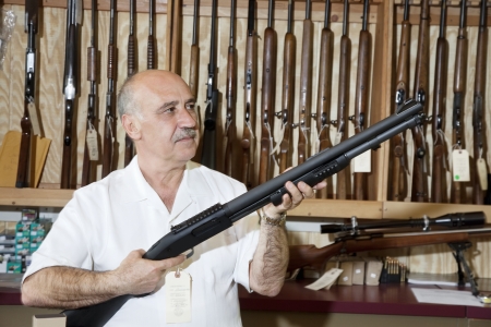 Mature gun store owner looking at weapon in shopの写真素材