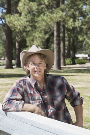 Mature man wearing cowboy hat leaning on wooden slabの写真素材