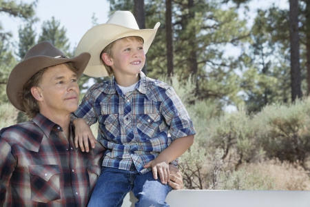 Mature father and son wearing cowboy hats looking away in parkの写真素材