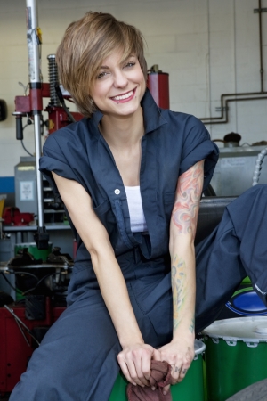 Portrait of a happy young female mechanic sitting on oil drum in car workshopの写真素材