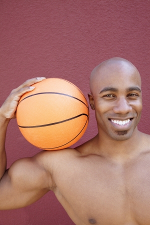 Portrait of a happy African American man with basketball on shoulder over colored backgroundの写真素材
