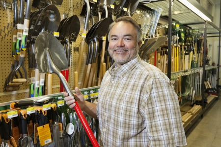 Portrait of a happy mature man holding shovel in hardware storeの写真素材