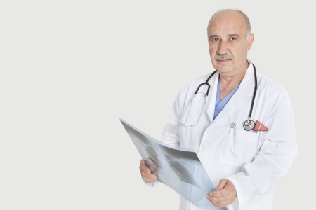 Portrait of senior male medical practitioner holding x-ray over gray backgroundの写真素材