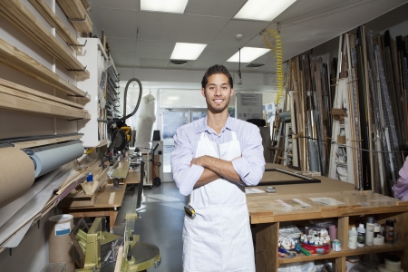 Portrait of a happy young craftsman standing with arms crossed in workshopの写真素材