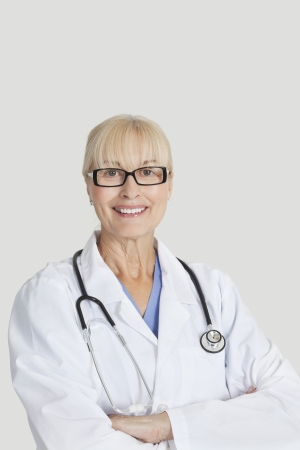 Portrait of senior female doctor with arms crossed over gray backgroundの写真素材