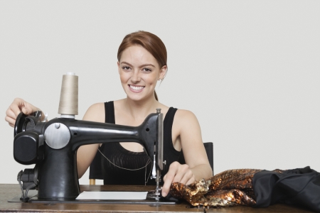 Portrait of young female tailor stitching cloth on sewing machine over colored backgroundの写真素材
