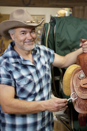 Portrait of a happy cowboy with riding tack in feed storeの写真素材