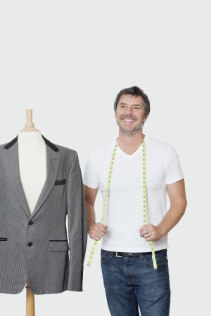 Mature male dressmaker standing next to tailor's dummy over gray backgroundの写真素材