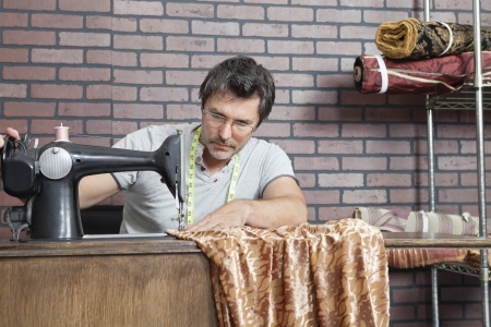 Mature male dressmaker stitching cloth on sewing machineの写真素材