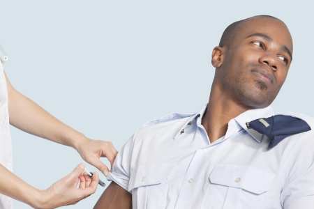 Young military man looking away as being injected by nurse over light blue backgroundの写真素材