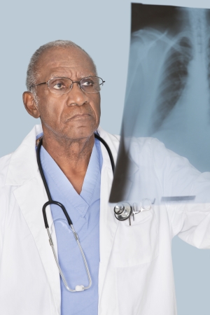 African American senor doctor analyzing x-ray report over light blue backgroundの写真素材