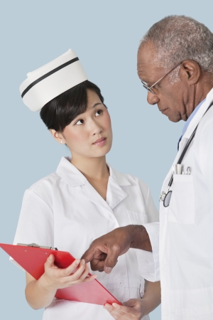 Two medical professionals having a discussion over medical report against light blue backgroundの写真素材