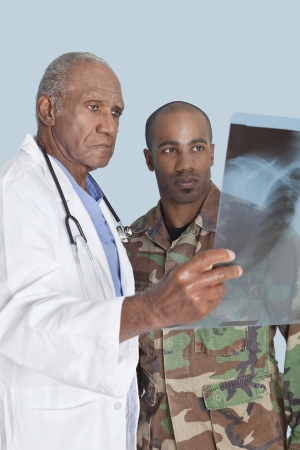 Senior doctor with US Marine Corps soldier looking at x-ray report over light blue backgroundの写真素材