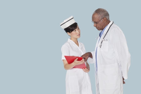 Two medical professionals in discussion over medical report against light blue backgroundの写真素材